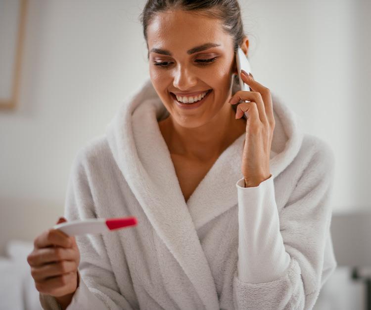 Smiling woman on the phone holding a pregnancy test