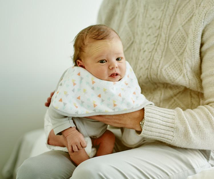 A baby wearing a patterned bib sitting on an adult's lap.