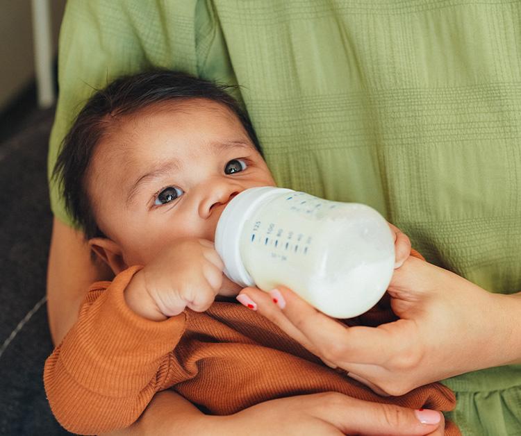 Baby drinking bottle in mother's arms