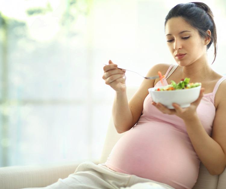 Pregnant mom sitting on the couch eating a salad