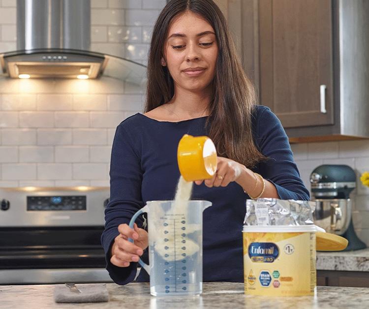 A person pouring formula powder into a measuring jug in a kitchen.