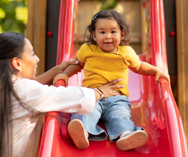 Mom helping toddler go down a slide