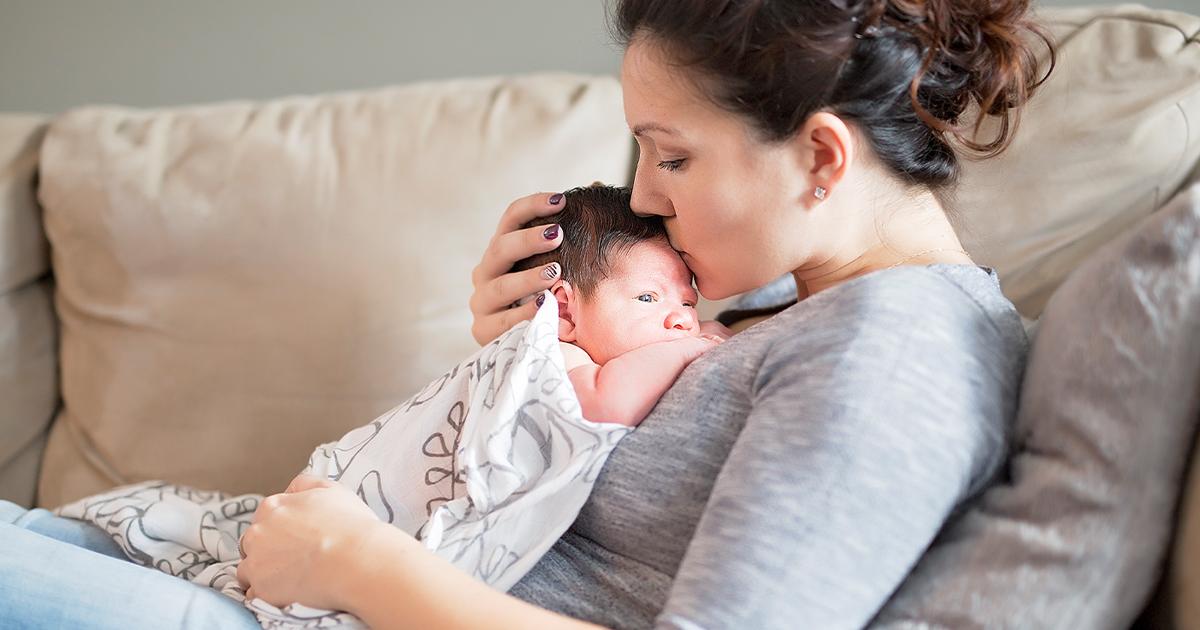 Madre sosteniendo tiernamente al bebé sobre su pecho, besando al bebé en la cabeza