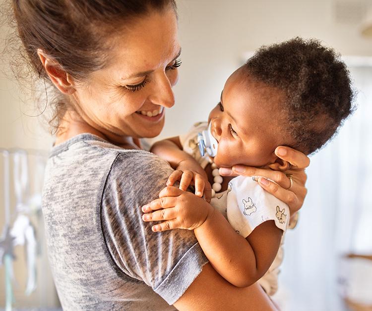 Baby with a pacifier being held by their mother