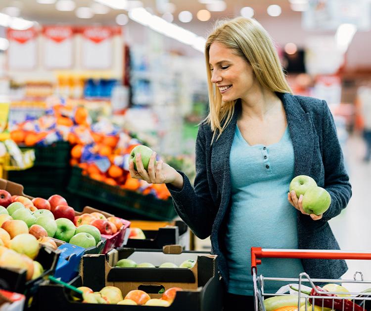 Pregnant woman grocery shopping holding green apples