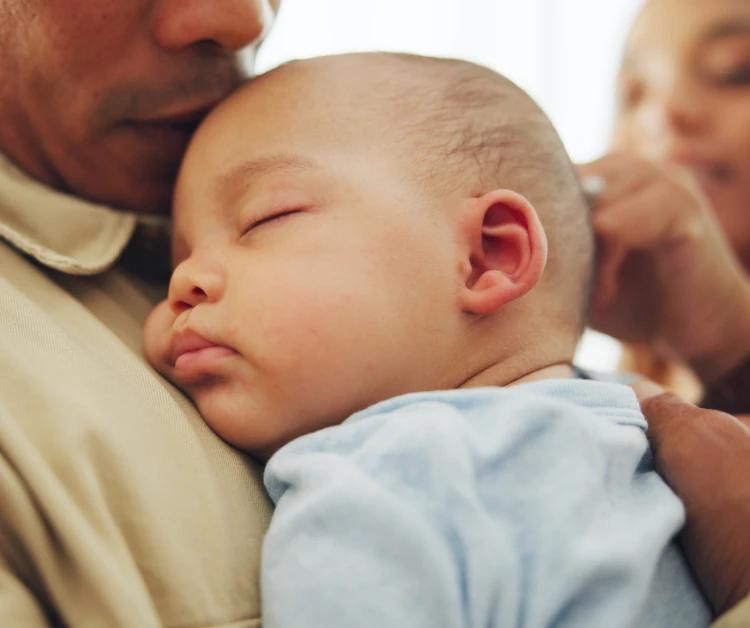 Bebé durmiendo mientras es sostenido por uno de sus padres.
