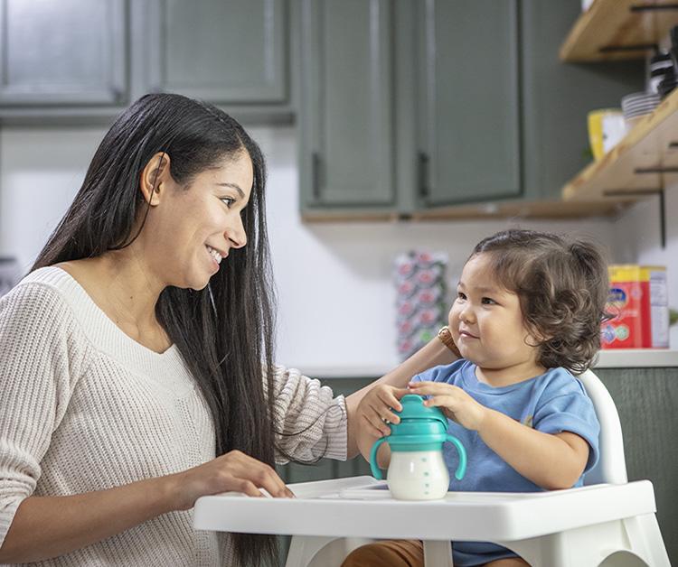 Mom smiling at baby in a highchair who has a milk bottle